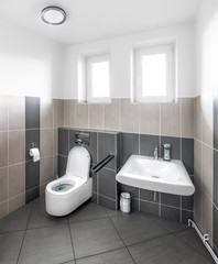 Small modernly furnished toilet with a sink and a variety of in-kind accessories and two windows lit in bright daylight.