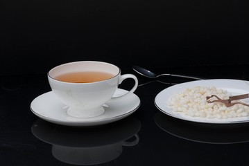 Granulated sugar in the shape of heart and cup of tea on black background