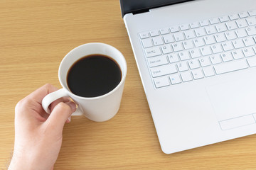 ノートパソコンを操作しながらコーヒーを飲む
