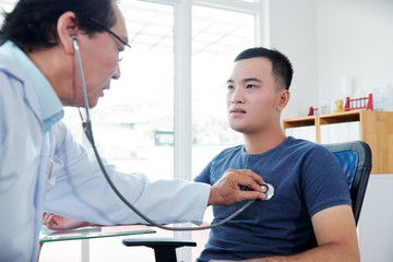 Fototapeta premium Doctor checking heartbeat of young man