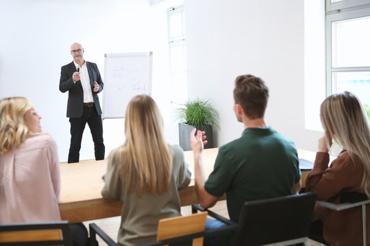 Junge Erwachsene hören einem älteren Vortragenden zu