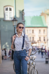 Woman in jacket and jeans walking on the street. Cheerful stylish woman with sunglasses outdoor. Woman wearing shades while looking away in the city street