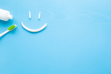 Toothbrush with green bristles, white tube of toothpaste on pastel blue background. Smiley face...
