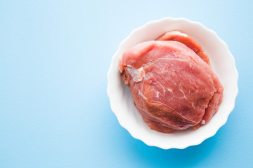 Red, raw, fresh meat fillet in white bowl on light pastel blue table. Empty place for text....