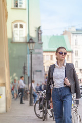 Woman in jacket and jeans walking on the street. Cheerful stylish woman with sunglasses outdoor. Woman wearing shades while looking away in the city street