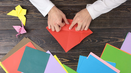 Male hands folding red paper sheet. Origami folding background. Japanese art of paper folding.