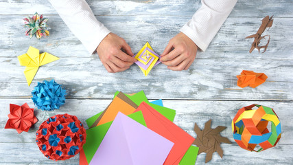 Man hands create beautiful origami toy. Collection of paper origami models on wooden table. Work,...