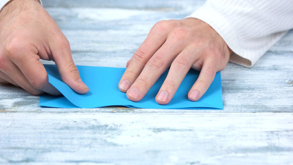 Close up hands folding blue paper sheet. Japanese paper folding workshop. Modern paper craft.