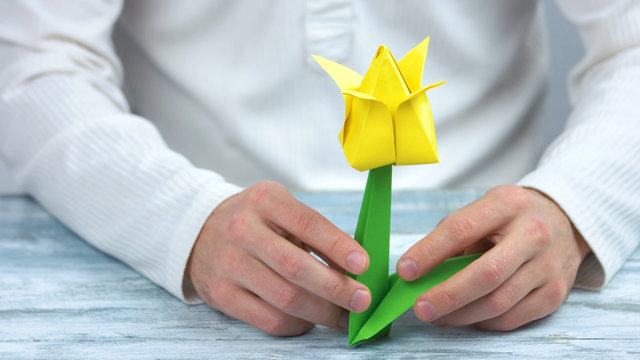 Male hands holding yellow origami tulip. Beautiful spring flower made from paper. Handmade gift for Womens or Mothers Day.