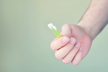 Male hand holding clean white cotton buds on blurred green background. Doctor holds sterile cotton bud for dna test. Man holding cotton buds for individual morning hygiene. Hygiene products