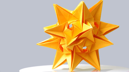 Stellated dodecahedron origami on grey background. Large yellow star paper figurine. Paper artwork...