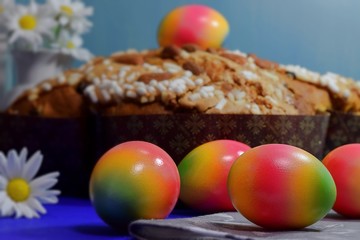 Easter egg on Easter pie, some other coloured eggs and chamomiles on blue background