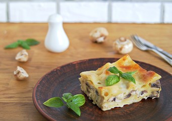 Portion of lasagna with chicken, mushrooms and mozzarella cheese on a brown clay plate. Italian сuisine. Selective focus.