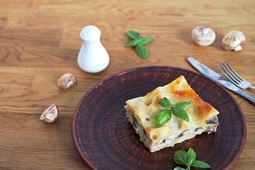 Portion of lasagna with chicken, mushrooms and mozzarella cheese on a brown clay plate. Italian сuisine. Selective focus.
