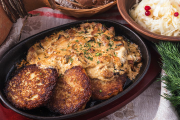 Potato pancakes with  sour cream sauce and mushrooms on a frying pan. Closeup