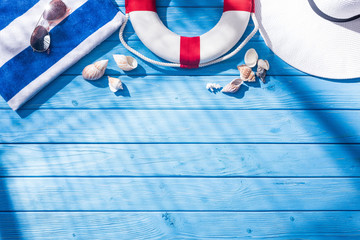 top view of striped towel, sunglasses, lifebuoy, white floppy hat and seashells on blue wooden...