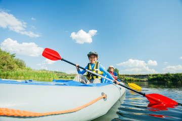 Happy kids kayaking on the river on a sunny day during summer vacation
