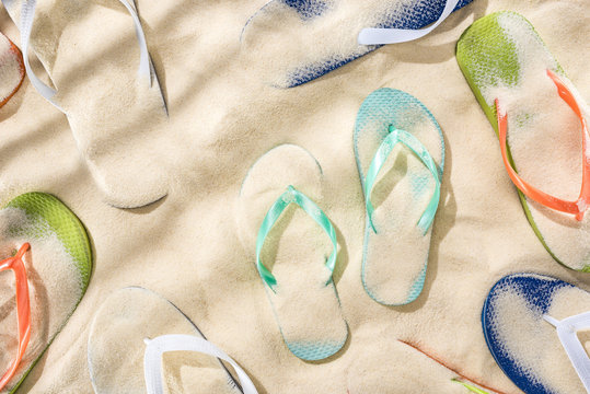 top view of scattered turquoise, orange, blue and green flip flops on sand