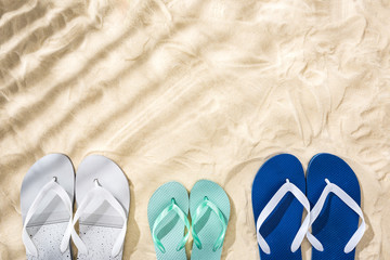 Fototapeta premium top view of white, turquoise and white blue flip flops on sand with shadows and copy space