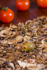 A piece of pizza with olive and mushrooms on a wooden table with tomatoes next to it
