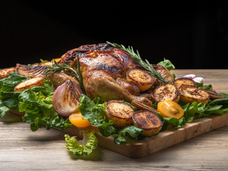 Roasted chicken with grilled potatoes and onion, yellow tomatoes, fresh green salad on wooden table. Owen cooked meat with vegetables. Original food serving in restaurant, cafe. Holiday dinner.