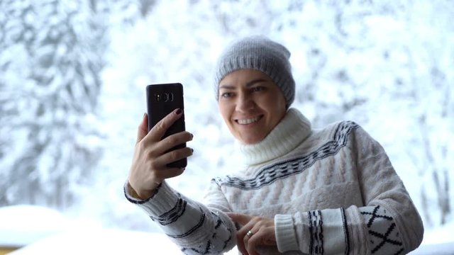 Young woman taking a self portrait with her smartphone in the snowy forest