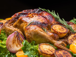 Roasted chicken with grilled potatoes and onion, yellow tomatoes, fresh green salad on wooden table. Owen cooked meat with vegetables. Original food serving in restaurant, cafe. Holiday dinner.