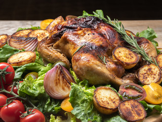 Roasted chicken with red and yellow tomatoes, grilled potatoes and onion pieces, fresh green salad on wooden surface. Owen cooked meat with vegetables. Original food serving. 