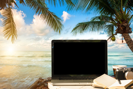 Mockup image of laptop with empty screen with camera,notebook,coffee cup on table with at landscape early morning sunrise over the sea,working on the beach,Freelance work and traveler concept.