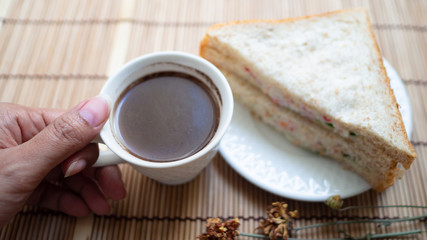 Hand holding cup black coffee with sandwiches placed in a white plate near