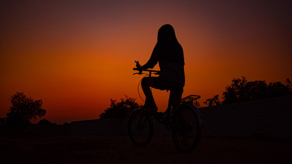 Fototapeta na wymiar Long haired girl Sitting on a bike Staring at the sunset, silhouette concept.