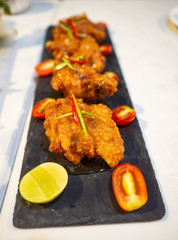 Crispy fried chicken placed in a long black dish, Served with lemon and tomato.