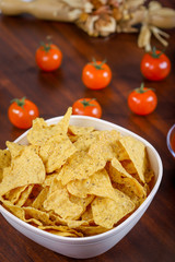 Yellow nacho in white bowl on the wooden table with tomato next to it