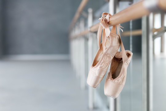 Pointe shoes hang on ballet barre in dance class room. Blurred background of ballet classic school.