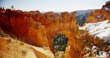 Vertical panning shot of red stone arch and snowy valley in 4K