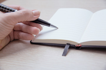 Top view of the table where there is a clean pocketbook. Women's left handed hold a pen and prepare to write something.