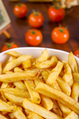 French fries in white bowl and tomato on wooden table