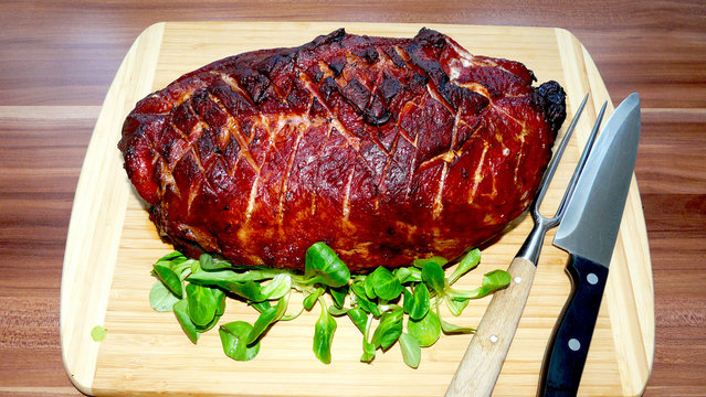 Kasseler Krustenbraten mit Rautenschnitt angerichtet mit Feldsalat auf einem Bambusholzbrett und  schr&auml;g angelegtem Tranchierbesteck