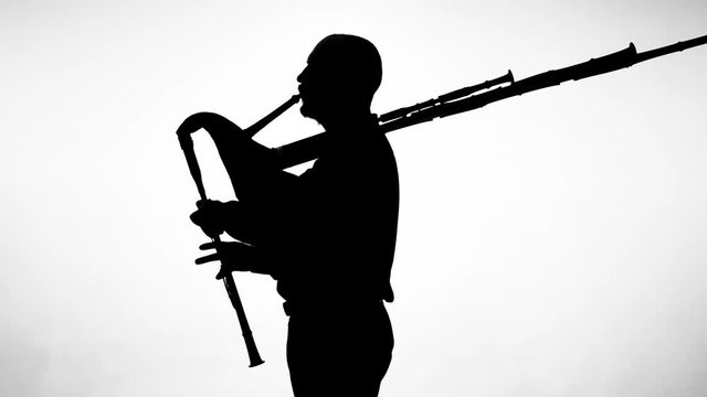 black silhouette on white background man playing bagpipes, national ethnic instrument close up