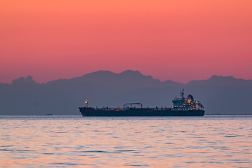 Cargo ship floating on the sea in the evening with the mountains n the background