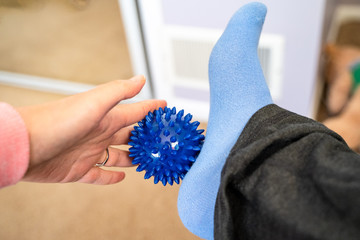 Woman with plantar fasciitis uses a spiky ball to massage her aching foot