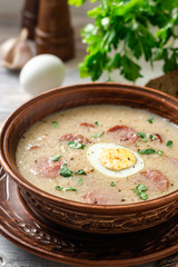 Traditional polish soup Zurek in ceramic bowl on wooden table. Selective focus.