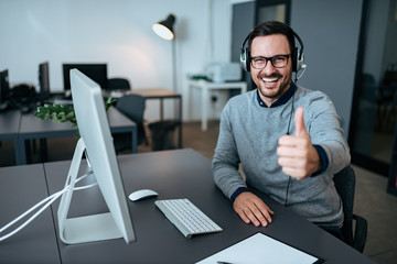 Cheerful male tech support manager showing thumbs up in office. - obrazy, fototapety, plakaty