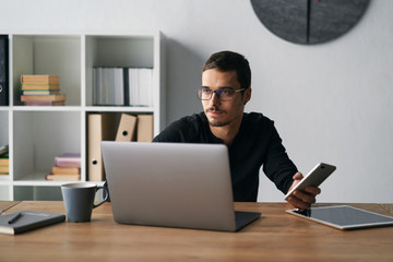 Young man working with phone and computer, receiving phone call, talking with partners 