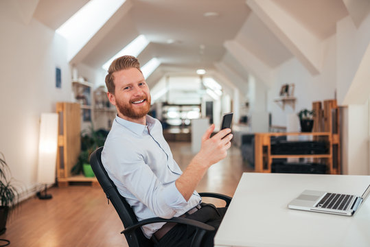 Smiling business man in bright office using phone.