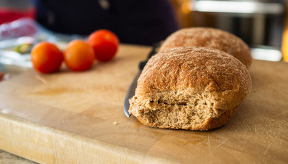 Bread rolls on a chopping board with tomatoes in the background