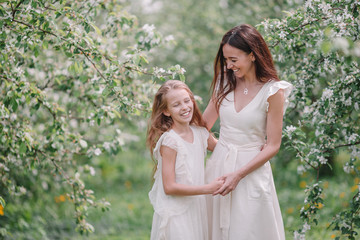 Adorable little girl with young mother in blooming cherry garden on beautiful spring day