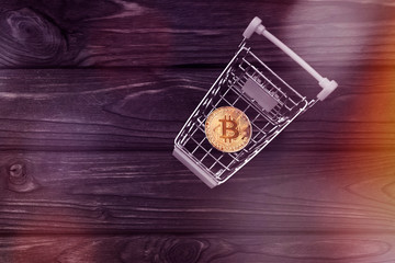 Bitcoin in the cart from the supermarket on the background of a wooden table. the Internet, a virtual currency. e-business.