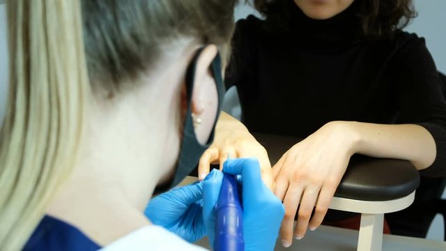 Manicurist girl pushes the cuticle apparatus with a corundum cone in the beauty salon
