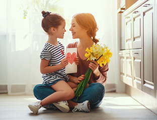 happy mother's day! child daughter   gives mother a bouquet of flowers to narcissus and gift.
